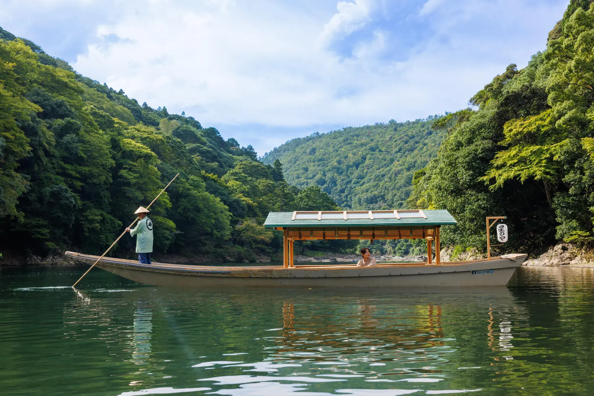 HOSHINOYA Kyoto's covered arrival boat crossing the Oi River below forested Arashiyama hills.