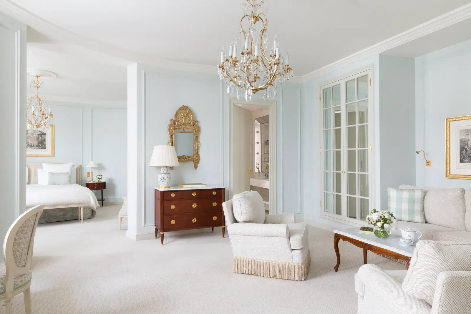 A Junior Suite Deluxe at Le Bristol Paris, a pale panelled room with a chandelier, upholstered seating and full-height windows onto the garden side