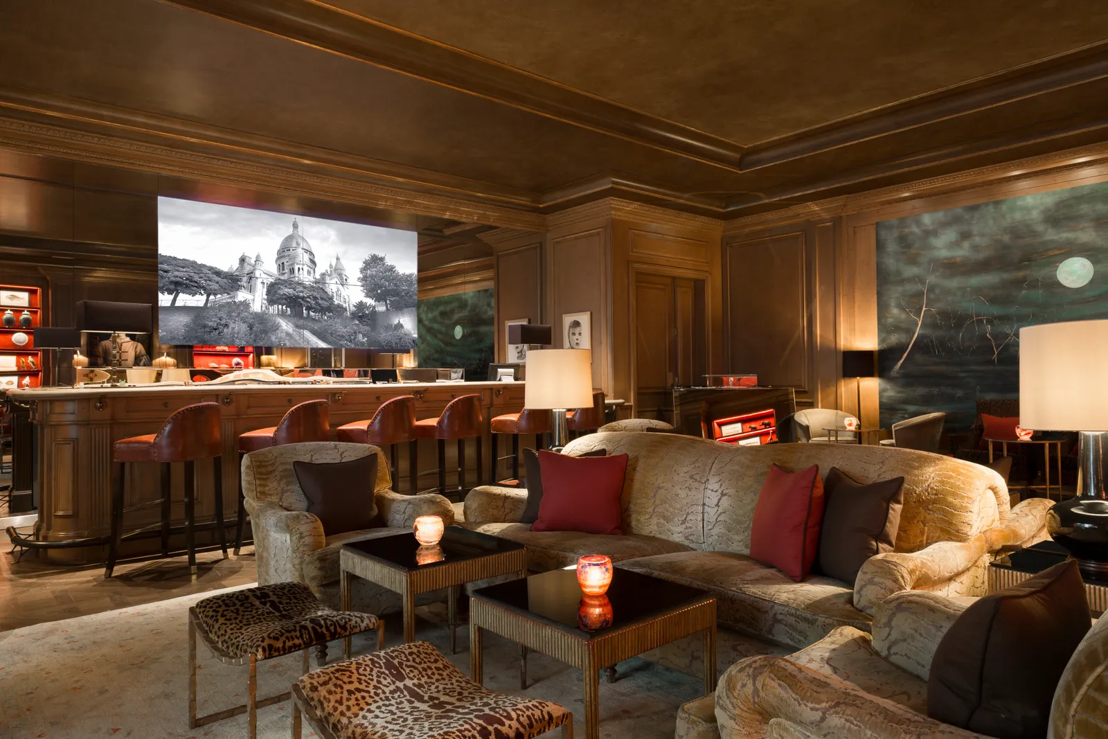 Le Bar du Bristol, a low-lit panelled room with leather bar stools along a wooden counter, velvet armchairs, leopard-print stools and a large black-and-white photograph of Sacré-Cœur