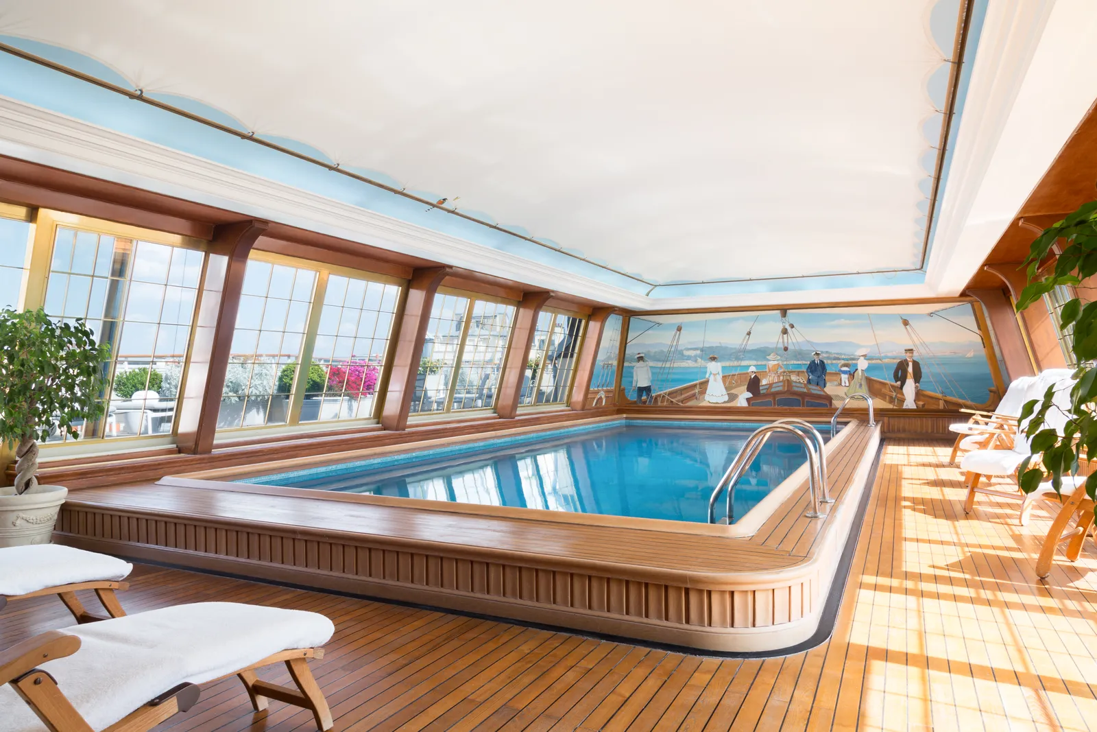 The rooftop pool at Le Bristol Paris, built like a yacht deck in varnished teak, with a painted sailing mural along one wall and steamer chairs on the boards