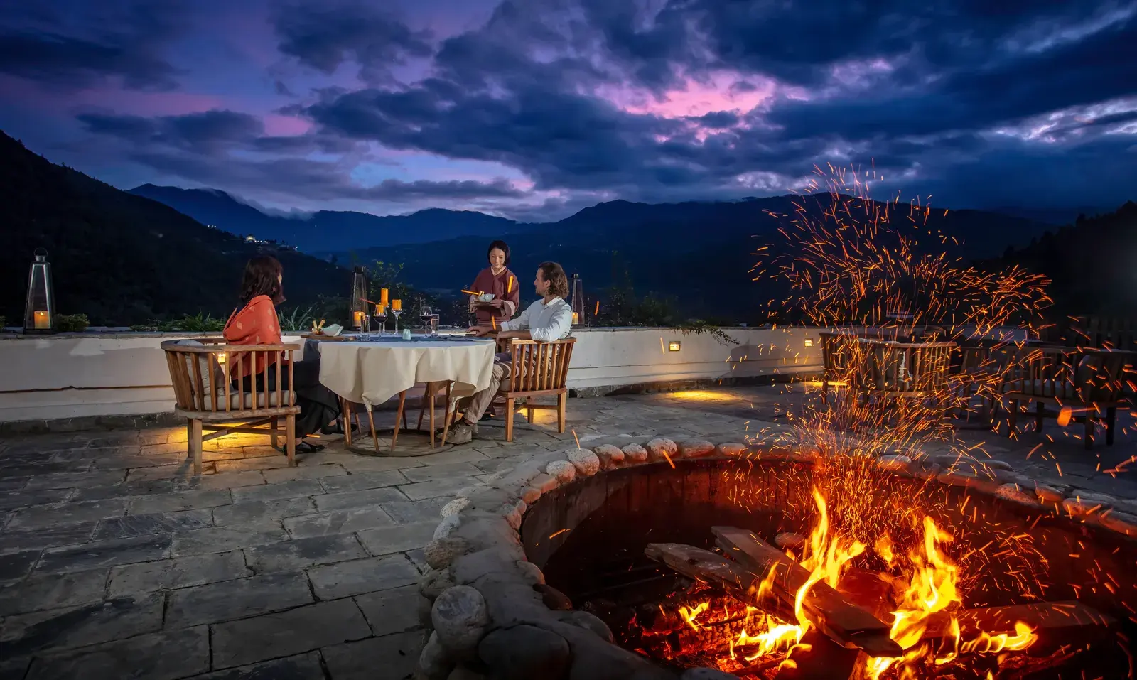 Outdoor dining terrace and fire pit at Bhutan Spirit Sanctuary overlooking the Paro valley at dusk
