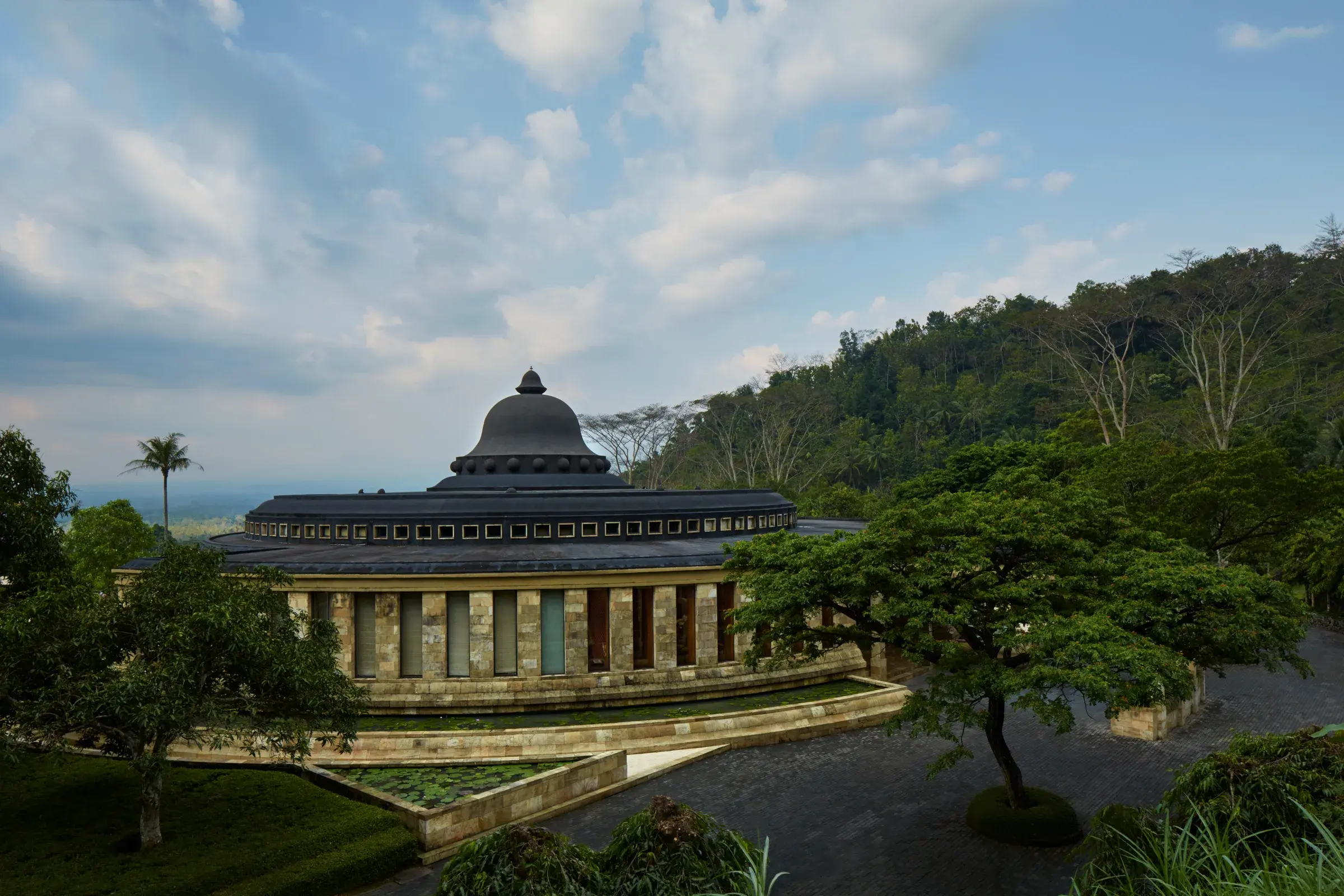 Amanjiwo's open-air limestone rotunda framing a distant view of Borobudur temple across the Kedu Plain.