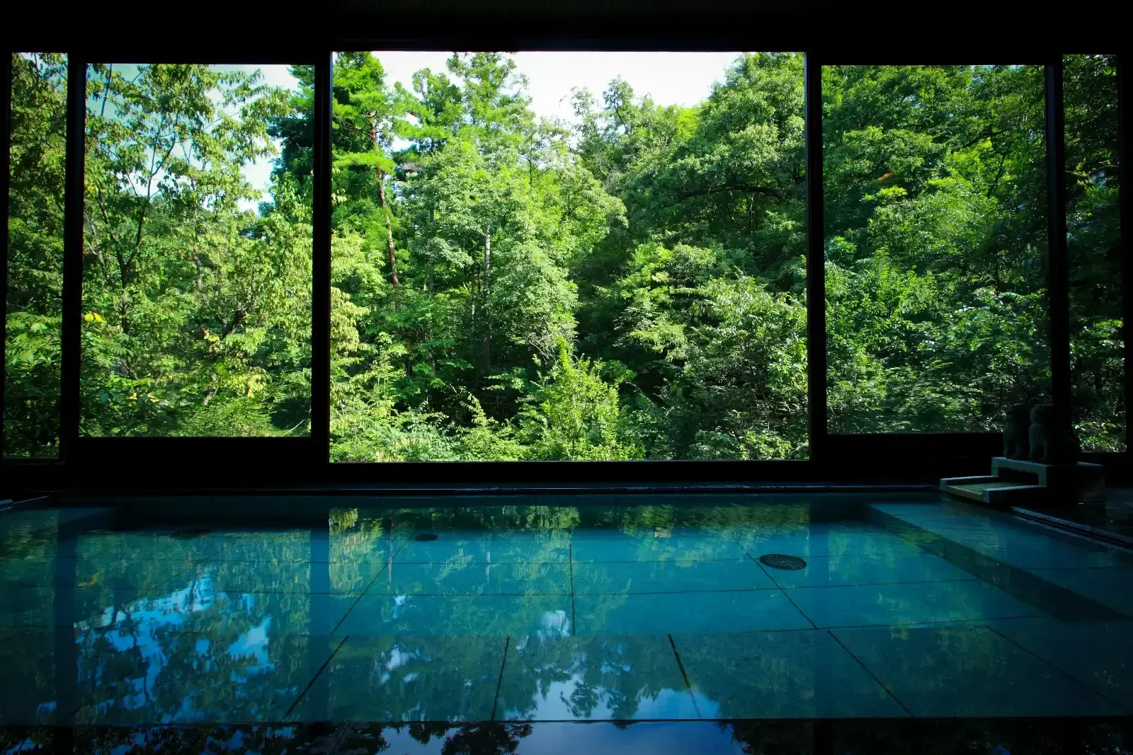 Kayotei's indoor onsen reflecting a forested Yamanaka landscape through wide windows.