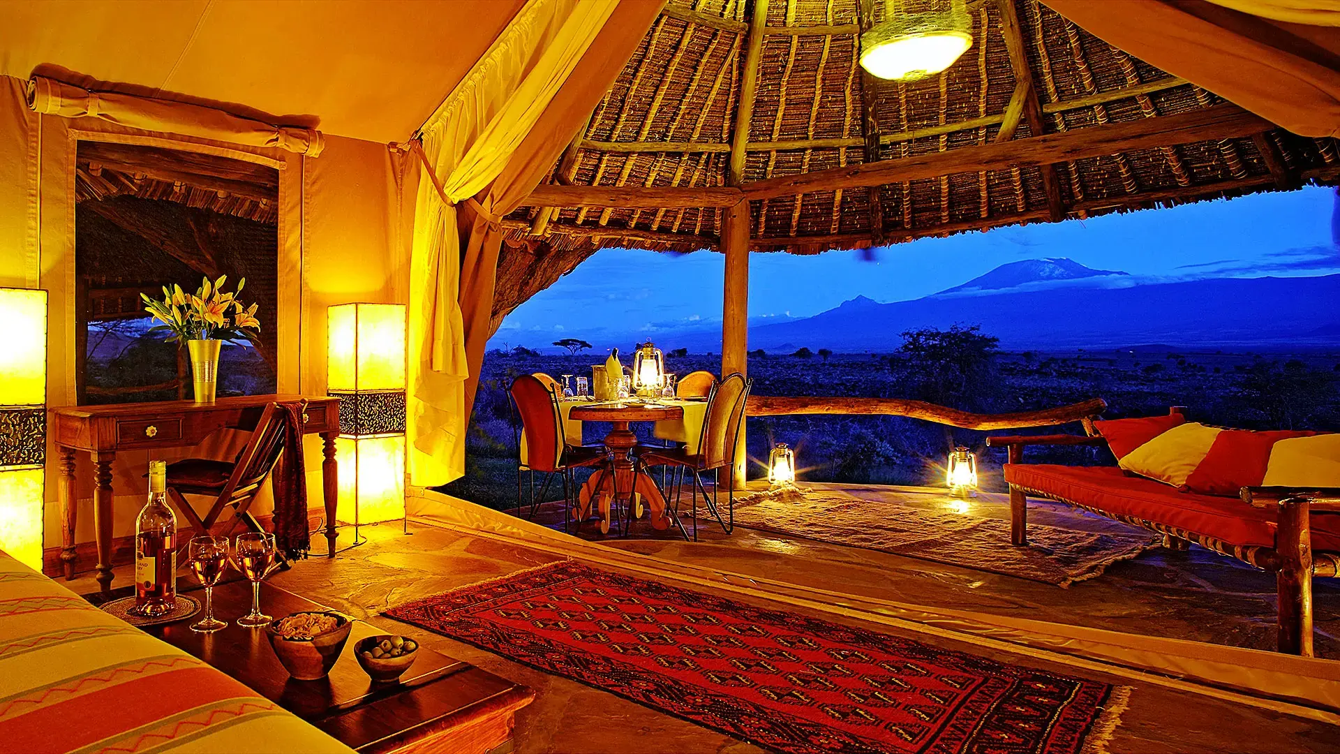A guest tent at Elewana Tortilis Camp Amboseli with a private dining setup on the deck and Mount Kilimanjaro visible at dusk.