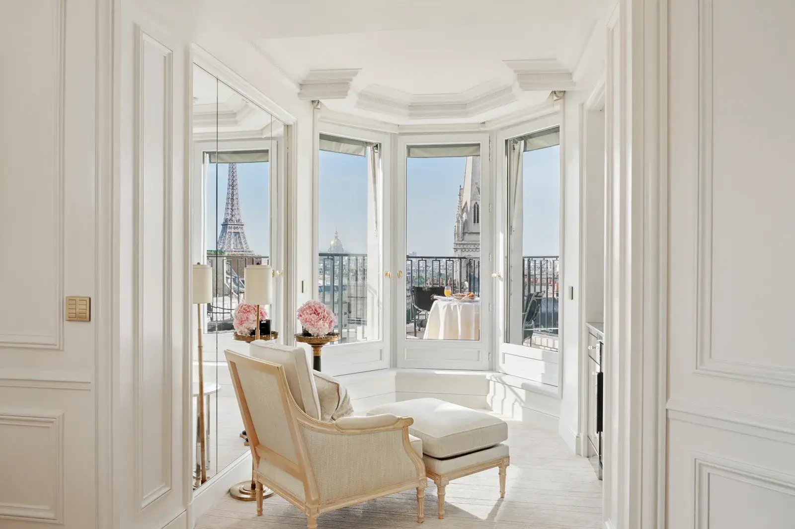 The Eiffel Tower Suite at Four Seasons George V, a pale bay-windowed sitting room with cream armchairs framing a direct view of the Eiffel Tower