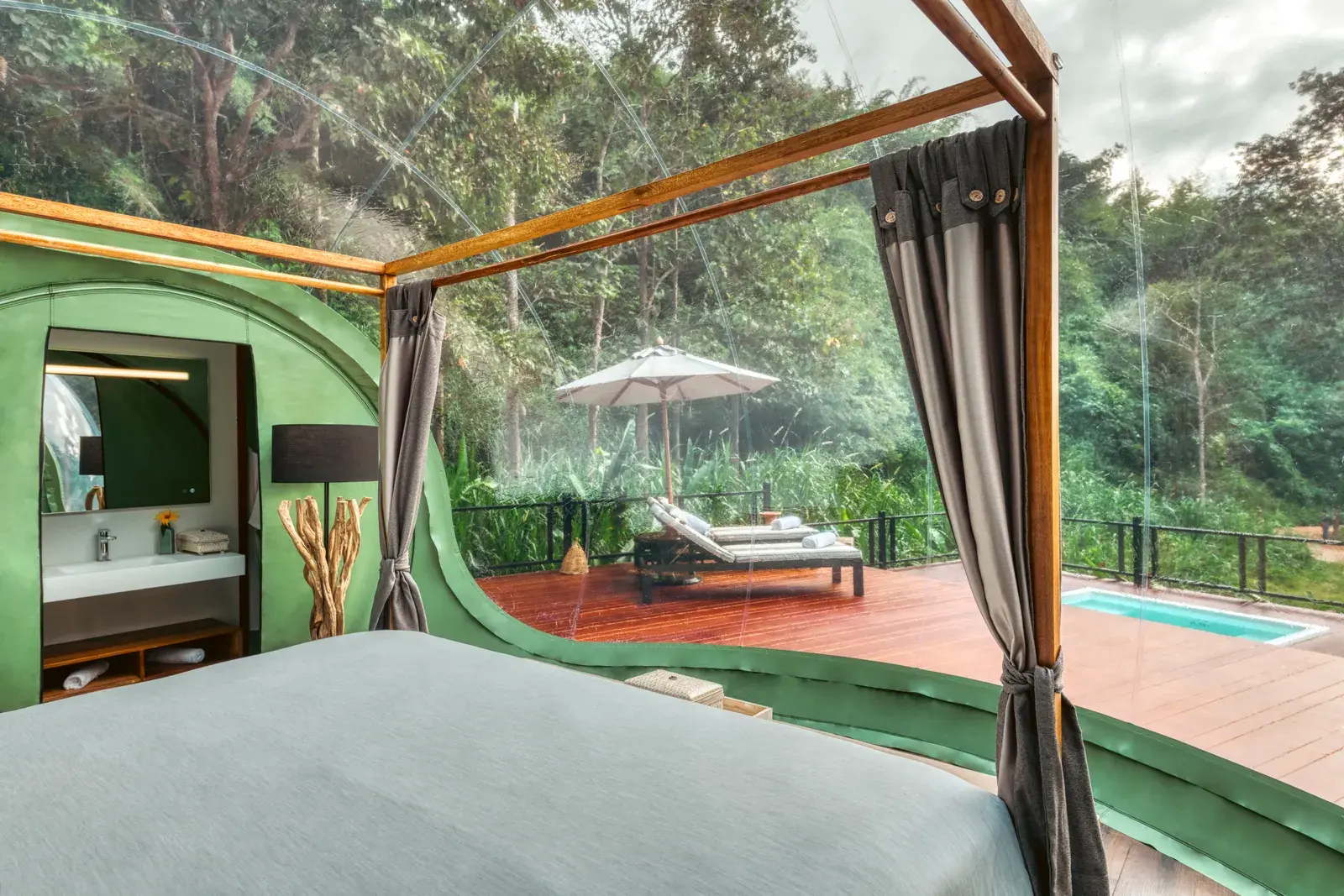 Inside a jungle bubble suite: the bed, open-plan bathroom, and private deck with pool and elephants visible beyond.